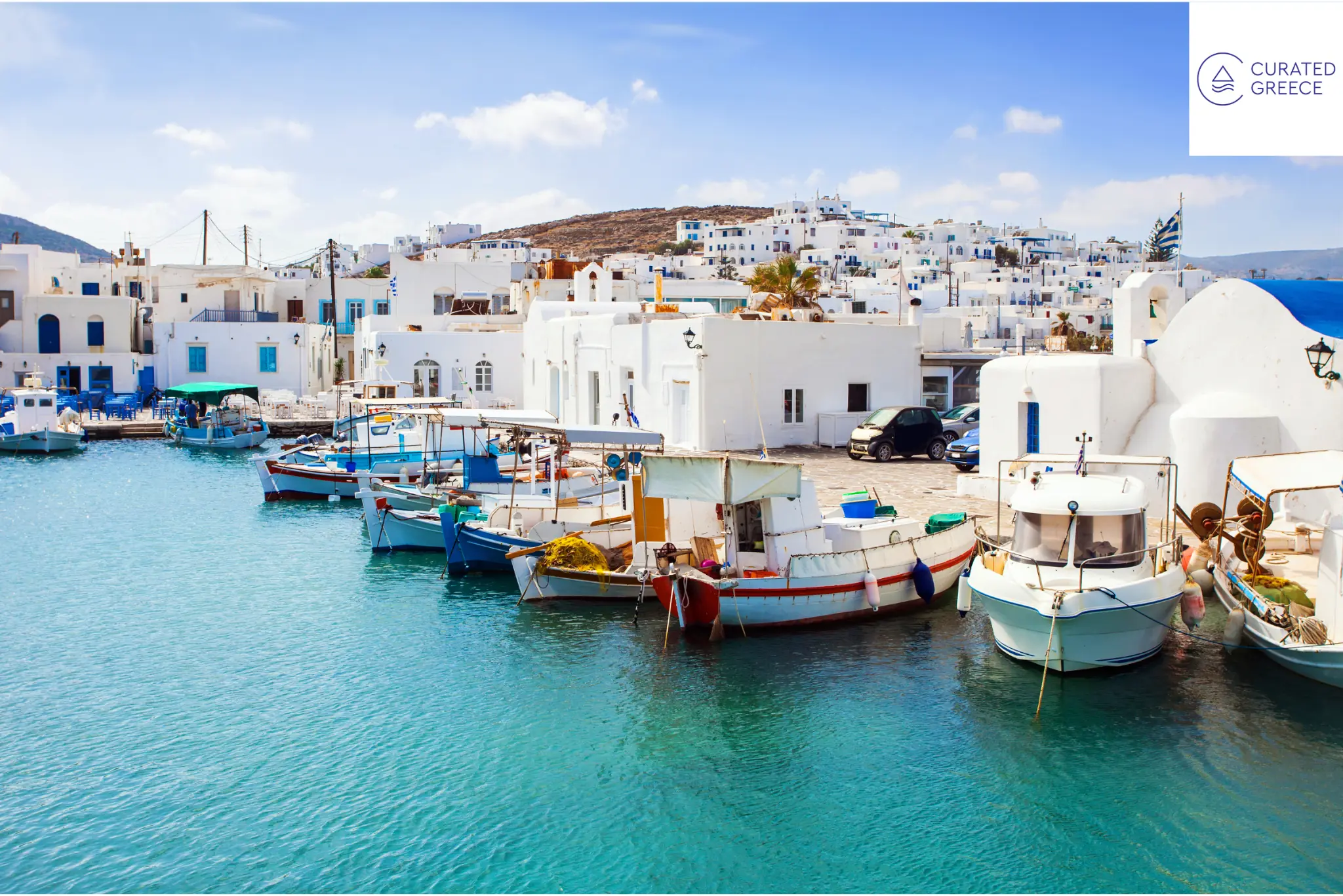 Boats moored in a turquoise Greek island harbor beside whitewashed buildings, with the Curated Greece logo.